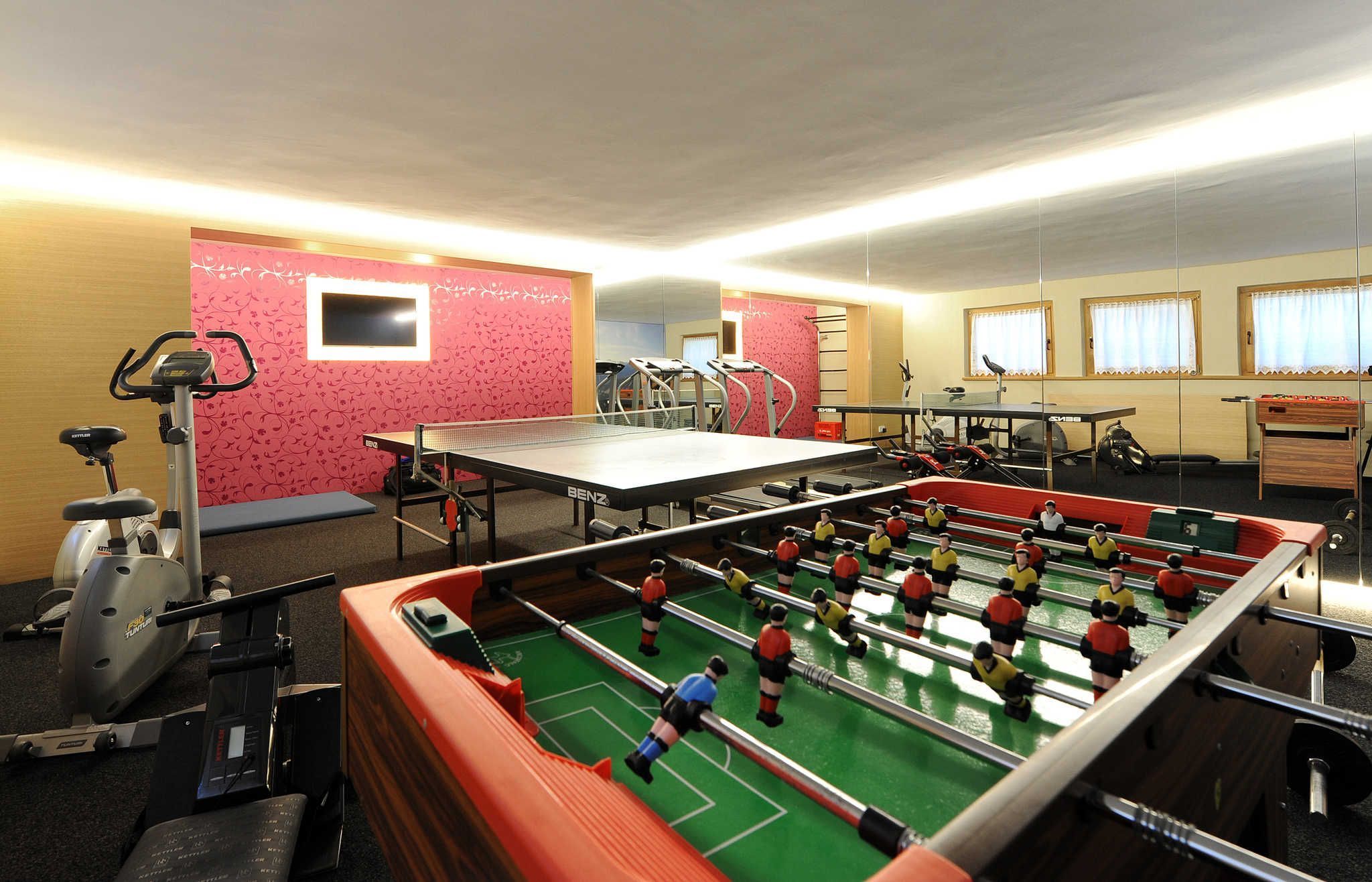 Una habitación con mesa de fútbol, equipo de ejercicio y mesa de ping pong.