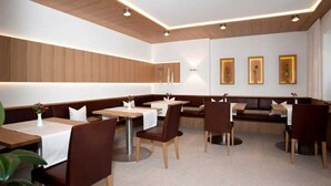 Ein Restaurant mit Sitzecken und Tischen, einer Holzbalkendecke und Wandleuchten.