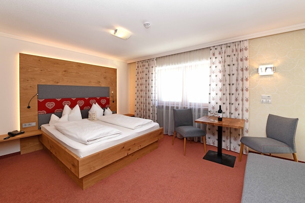A hotel room with a wooden bed, a desk with a chair, and a window with curtains.