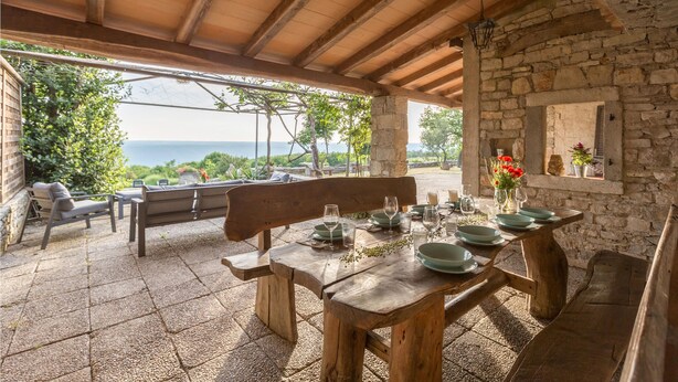 An outdoor dining area with a wooden table set for four, stone walls, and a view of the sea. - 3 bedroom stunning home in Gora Glusic (Gora Glusic)