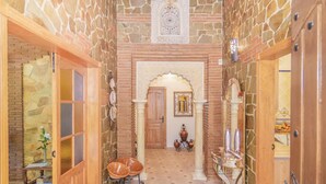 A narrow hallway with stone walls, wooden doors, and a central archway.