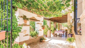A covered patio with a table set for dining, surrounded by potted plants and a pergola with vines.