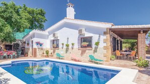 A pool area with a clear blue pool, outdoor seating, and a white building with stone accents.