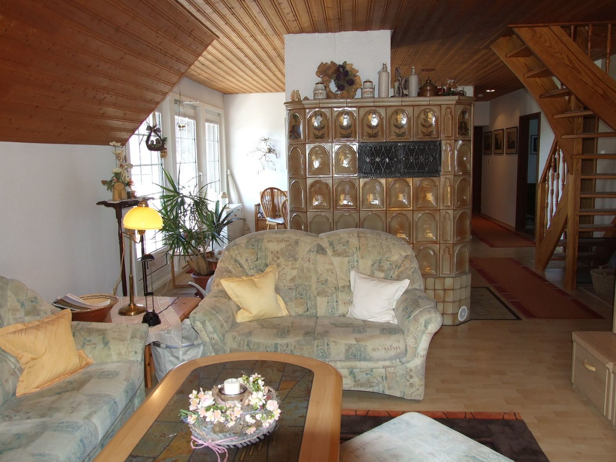 A cozy living room with a patterned sofa, a coffee table with a floral centerpiece, and a wooden staircase.
