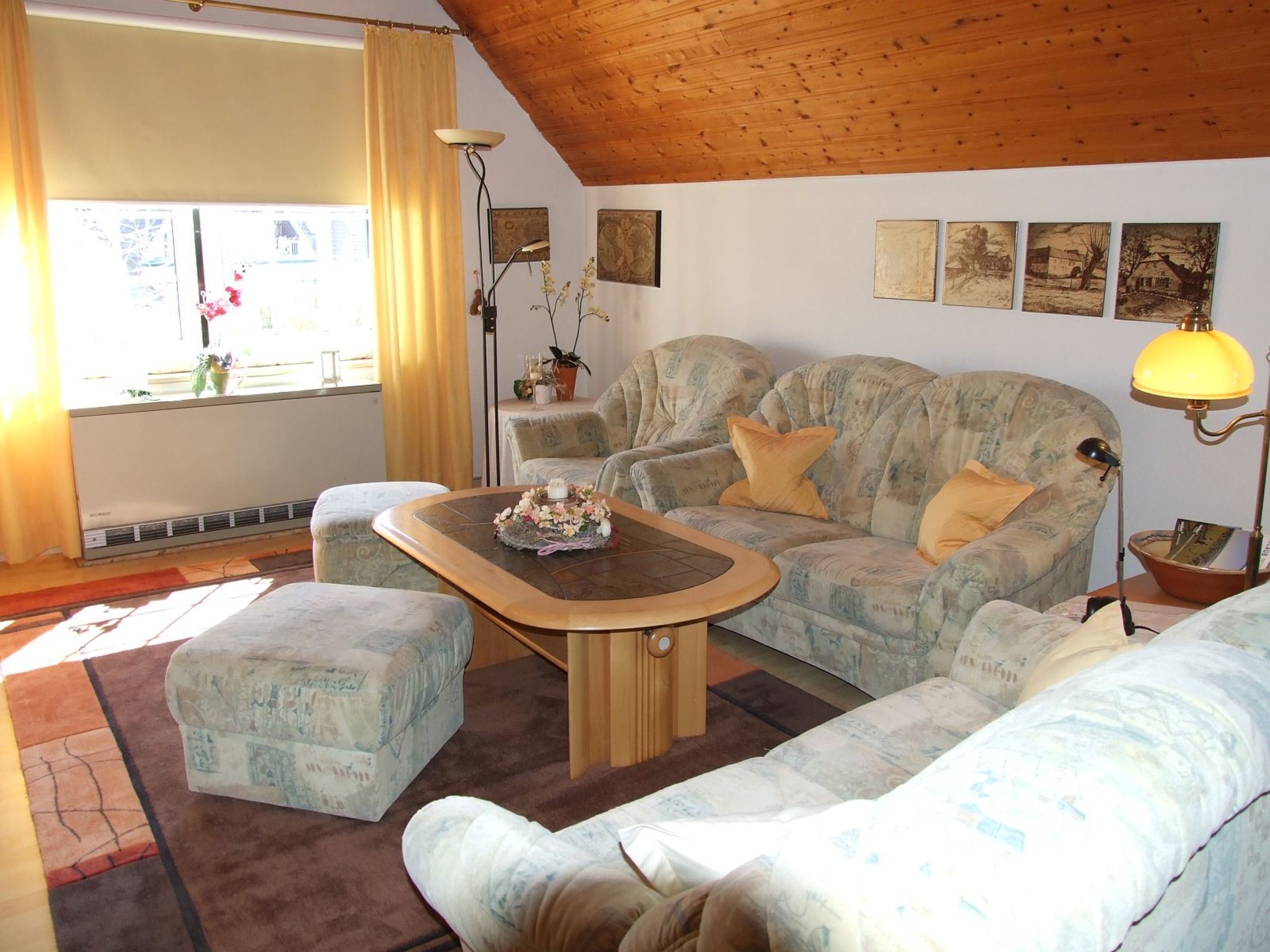 A cozy living room with a wooden ceiling, a sofa, a coffee table, and a window with curtains.