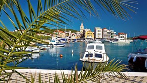 Uma marina com barcos atracados, céu azul claro e edifícios com telhados vermelhos ao fundo.