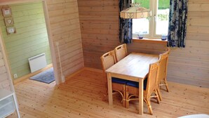 Ein Holzinnenraum mit einem Esstisch, Stühlen, einem Heizkörper und einem Fenster mit Vorhängen.