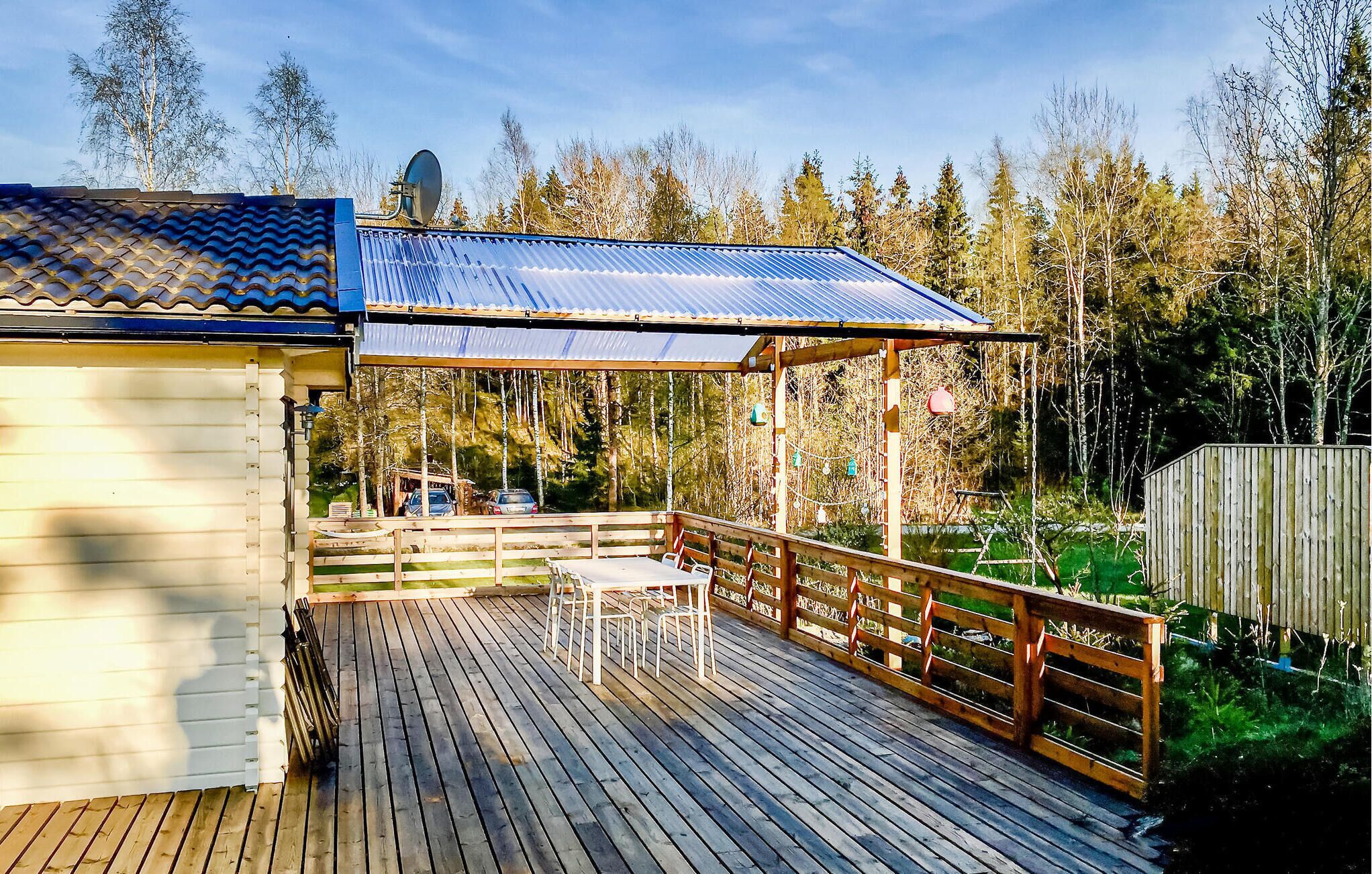 Une terrasse en bois avec un espace patio couvert, un petit bâtiment doté d’un toit en tuiles et une cour clôturée avec des arbres.
