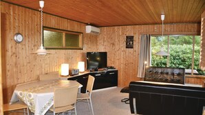 A cozy cabin interior with a dining table, chairs, a sofa, a television, and a window with a view of greenery. - 3 bedroom stunning home in Kirke Hyllinge (Kirke Hyllinge)