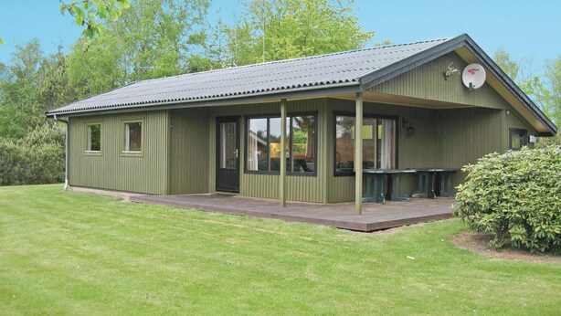 A green building with a covered patio, large windows, and a small outdoor seating area. - 3 bedroom stunning home in Kirke Hyllinge (Kirke Hyllinge)