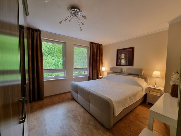 A hotel room with a bed, two bedside tables, a ceiling light fixture, and two windows with curtains.