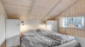 Un dormitorio con una cama, dos armarios blancos, un ventanal con cortinas y vigas de madera en el techo.