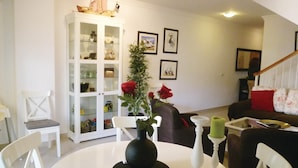 Ein Wohnzimmer mit einem weißen Schrank, einem Esstisch mit einer Vase und Kerzen sowie einer Treppe im Hintergrund.
