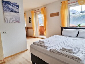 A hotel room with a bed, a window with a mountain view, a coat rack, and a door leading to an outdoor area.