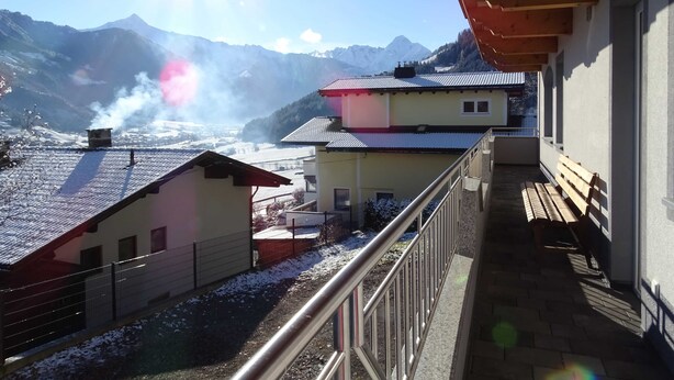 Une vue sur la montagne depuis un balcon doté d’une rambarde en métal, d’un banc en bois et d’un bâtiment avec un toit rouge.