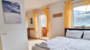 Une chambre d’hôtel comprenant un lit, une fenêtre donnant sur les montagnes, un porte-manteau et une porte donnant accès à un espace extérieur.
