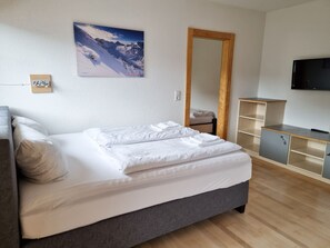 A neatly made bed with white linens, a large mirror, a television on the wall, and a wooden floor. - Apartment for 2-5 people - Alpine jewel (Laimach)