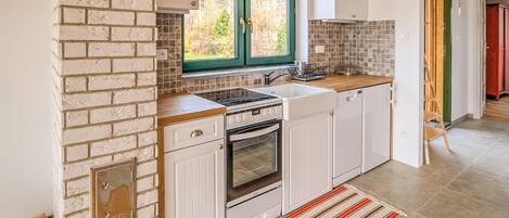 A kitchen with white cabinets, a stove, and a window with green shutters.