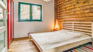 Una camera da letto con una parete in legno a tronchi, un letto con testiera bianca e una finestra con cornice verde.