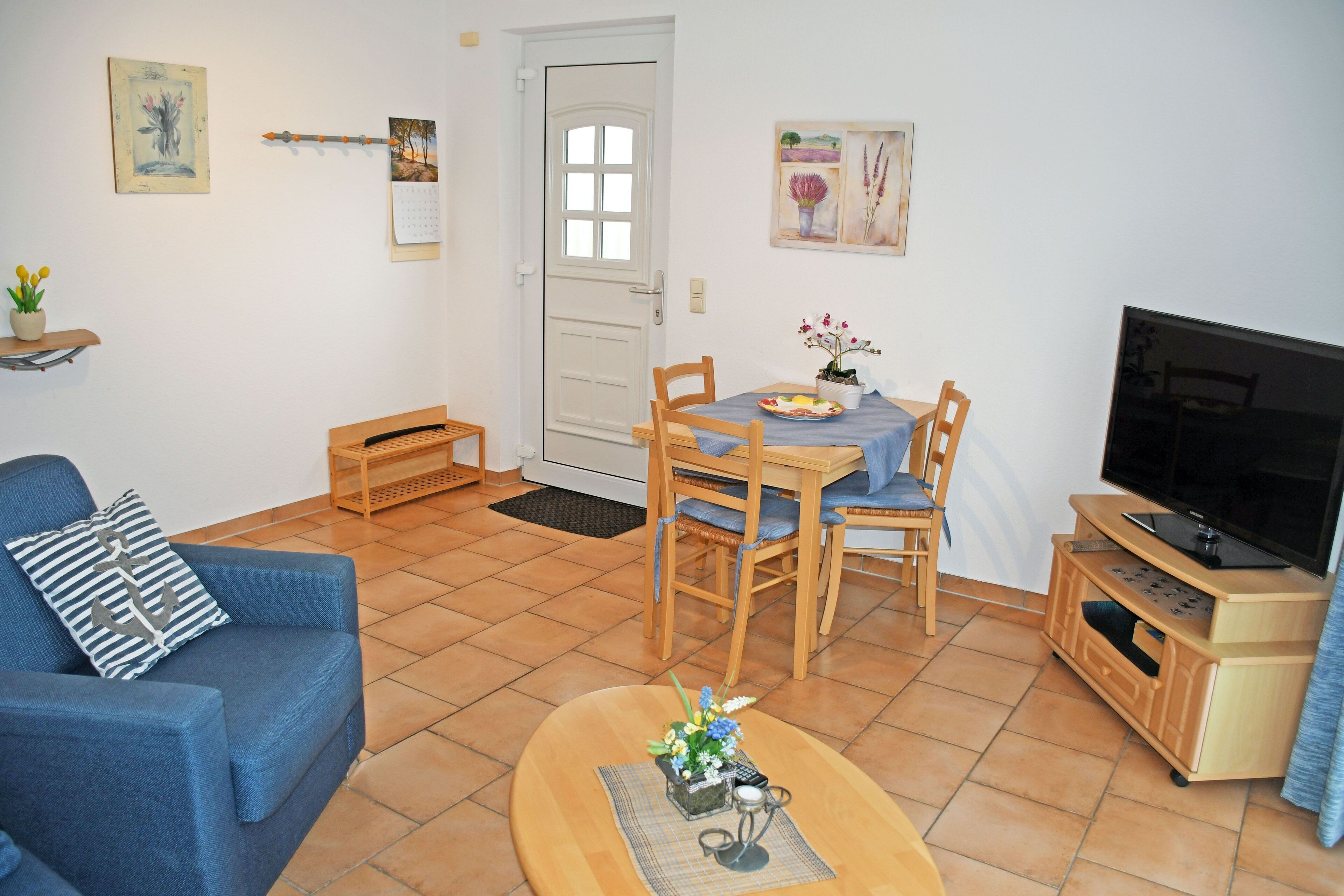A living room with a blue sofa, wooden dining table, chairs, a TV stand, and a small table with a plant.