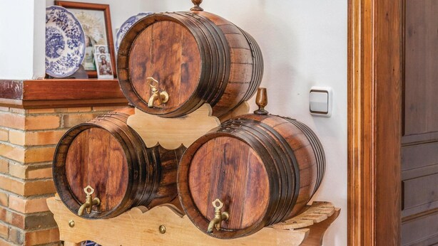 A wooden barrel rack with three barrels, a brick wall, and a door in the background.