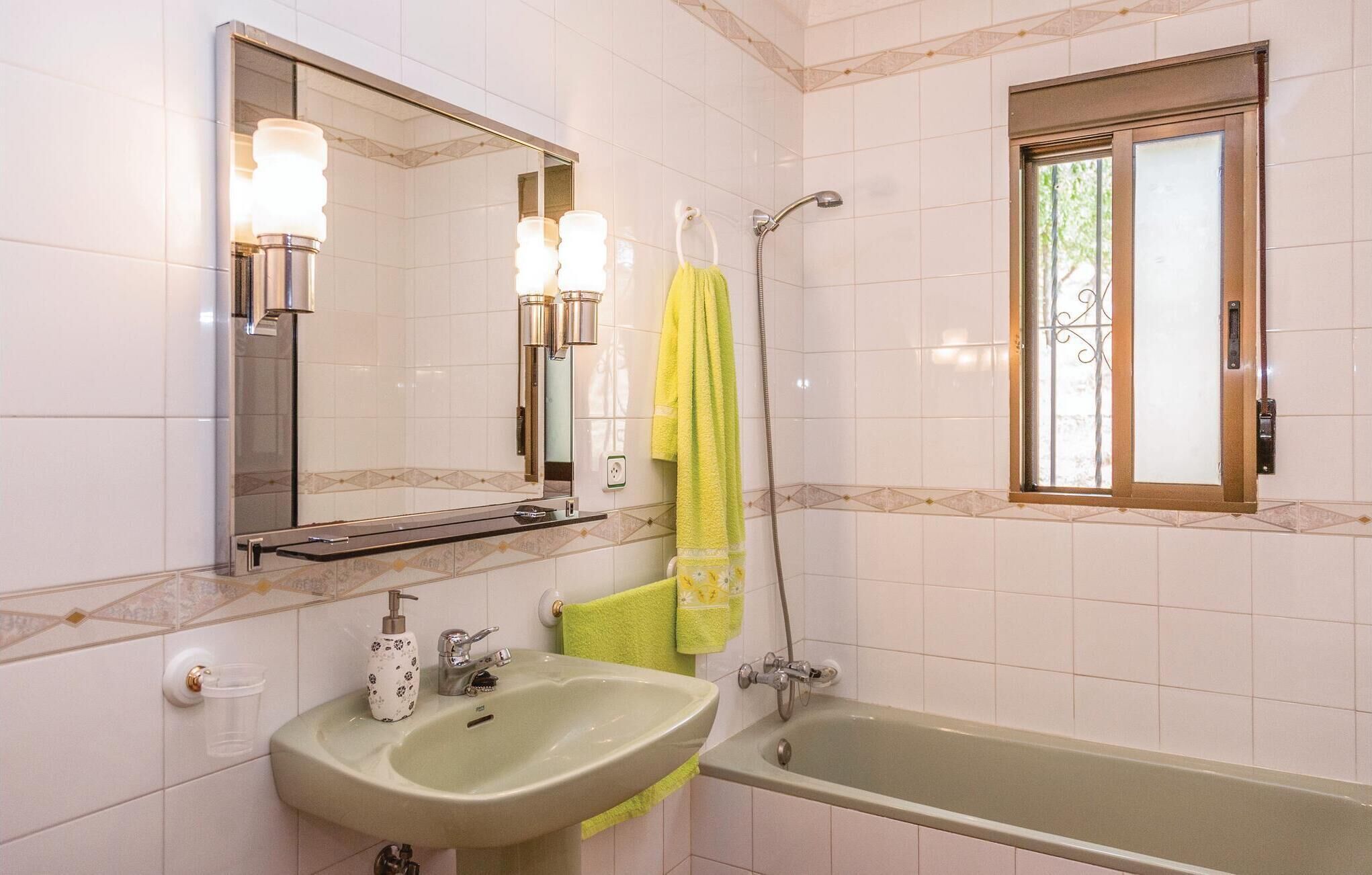 A bathroom with a sink, mirror, shower, and window.