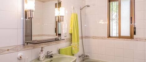 A bathroom with a sink, mirror, shower, and window.