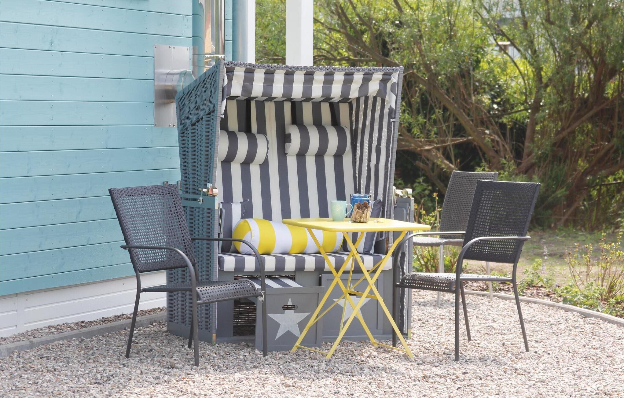 A small outdoor seating area with a striped chair, a yellow table, and a grey bench.