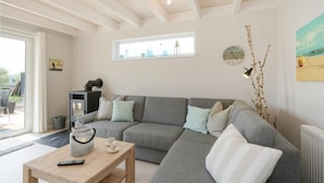 A cozy living room with a grey sectional sofa, a wooden coffee table, and a glass candle holder. A window provides natural light, and a clock is visible on the wall. - Gorgeous home in Süssau/Ostsee with sauna (Süssau/Ostsee)