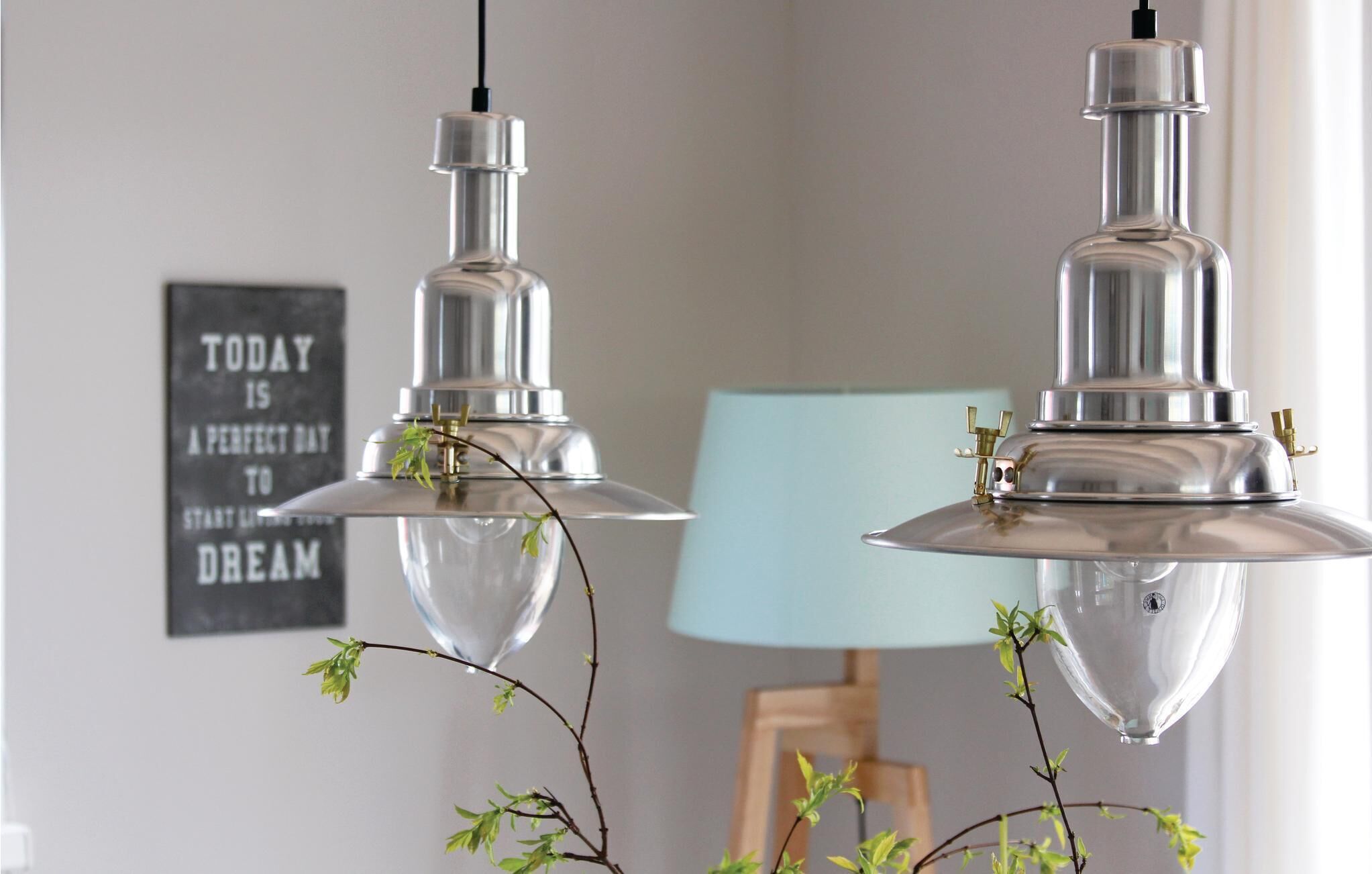 Two metallic pendant lights with clear glass shades and a small branch with green leaves hanging from them.