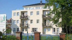 A multi-story residential building with balconies, a gated entrance, and a signboard. - Villa Aquamarina Whg. 8, TERRACE, CAR CHAIR - Villa Aquamarina, 1st ROW, partly. (Heringsdorf)