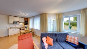 A compact living space with a kitchenette, a dining area, and a sofa with cushions. - Villa Aquamarina Whg. 8, TERRACE, CAR CHAIR - Villa Aquamarina, 1st ROW, partly. (Heringsdorf)