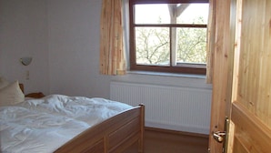 A bedroom with a wooden bed, a window with curtains, a radiator, and a door. - HIMME - Farmhouse Büchsenschütz (Vöhl)