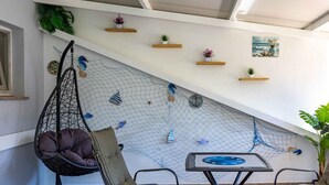 Une pièce avec un plafond en pente, un fauteuil suspendu, une table dont le plateau est bleu et des étagères murales ornées de plantes.