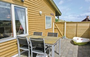 Et træhus med en terrasse, et bord, stole, en skydedør og en lille båd.