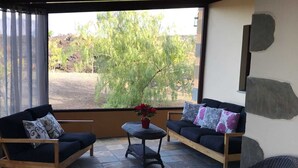 Eine sonnendurchflutete Terrasse mit zwei Sofas, einem kleinen Tisch mit einem Topfpflanzen und einem Korbstuhl.