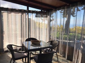 A dining area with a glass table and wicker chairs, a woven basket on the table, and a view through sheer curtains. - Casa Cueva de las Palomas (Los Llanos)