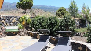 Eine Terrasse mit zwei Liegestühlen, einer Steinmauer und Blick auf eine Berglandschaft.