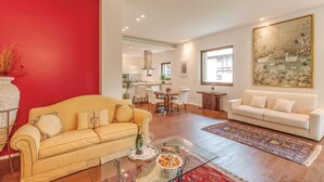 Una sala de estar con un sofá amarillo, un sofá blanco, una mesa de centro de vidrio y una pared de acento roja.