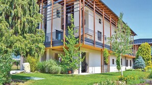 Un edificio moderno de varios pisos con un balcón, rodeado de vegetación exuberante y un jardín cuidado.