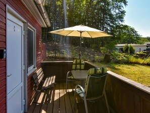 A wooden deck with a table and chairs, an umbrella, and a door to a red building.