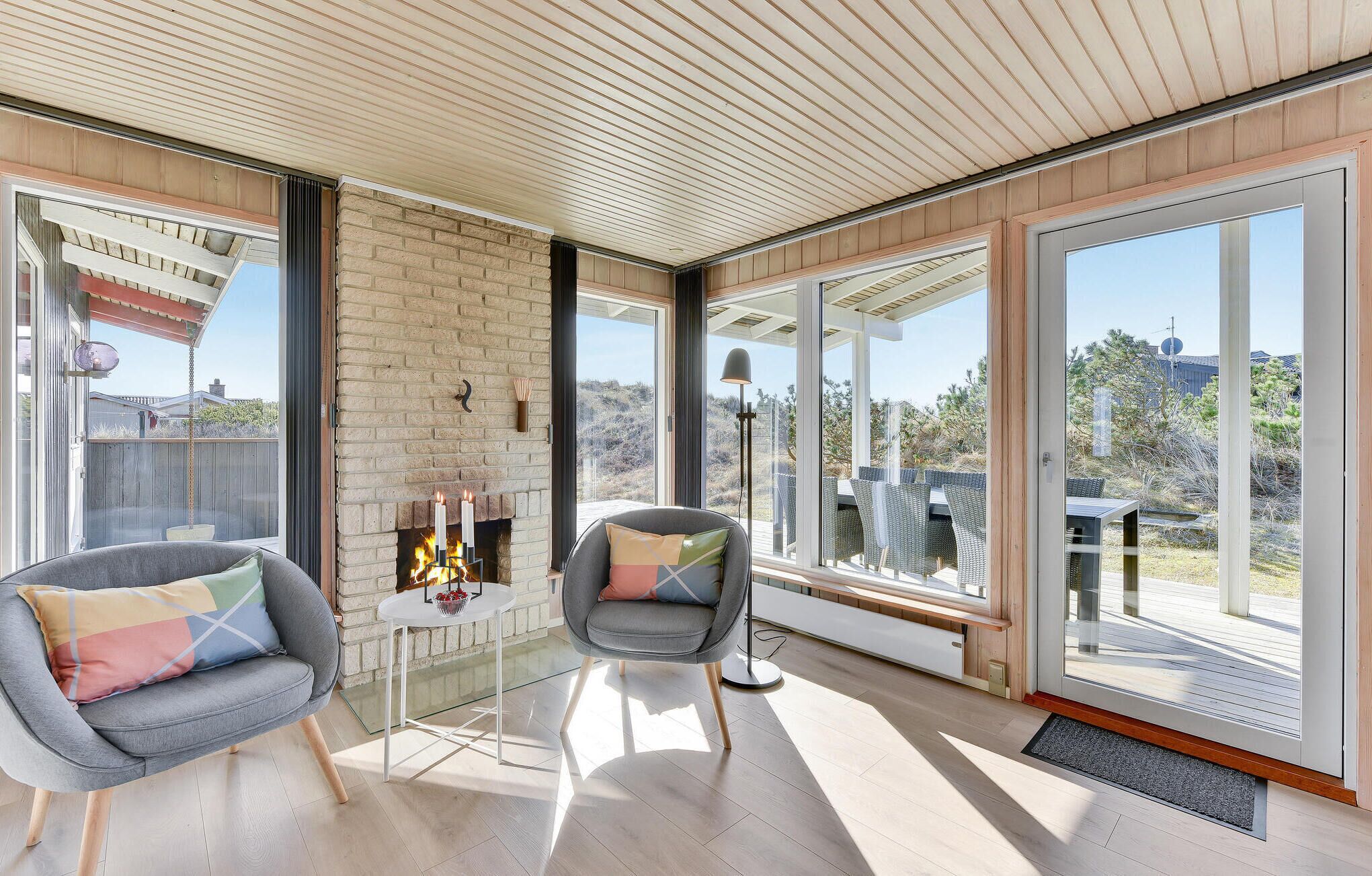 A modern living room with a fireplace, two grey armchairs, and a glass coffee table.