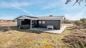 Ett envåningshus i trä med ett sluttande tak, en veranda med en bänk och en liten uteplats.