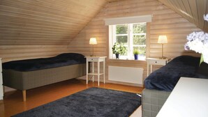 A cozy attic bedroom with two beds, a small table, and a window with a view of greenery.