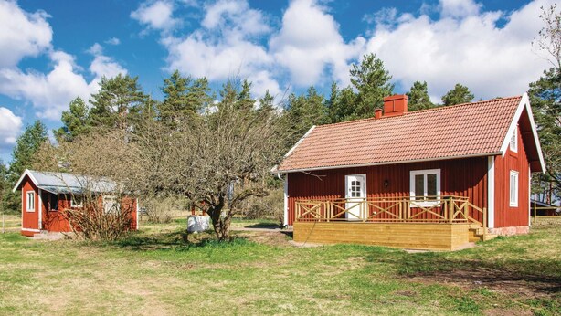 Two red wooden houses with a wooden deck, surrounded by trees and grass.
