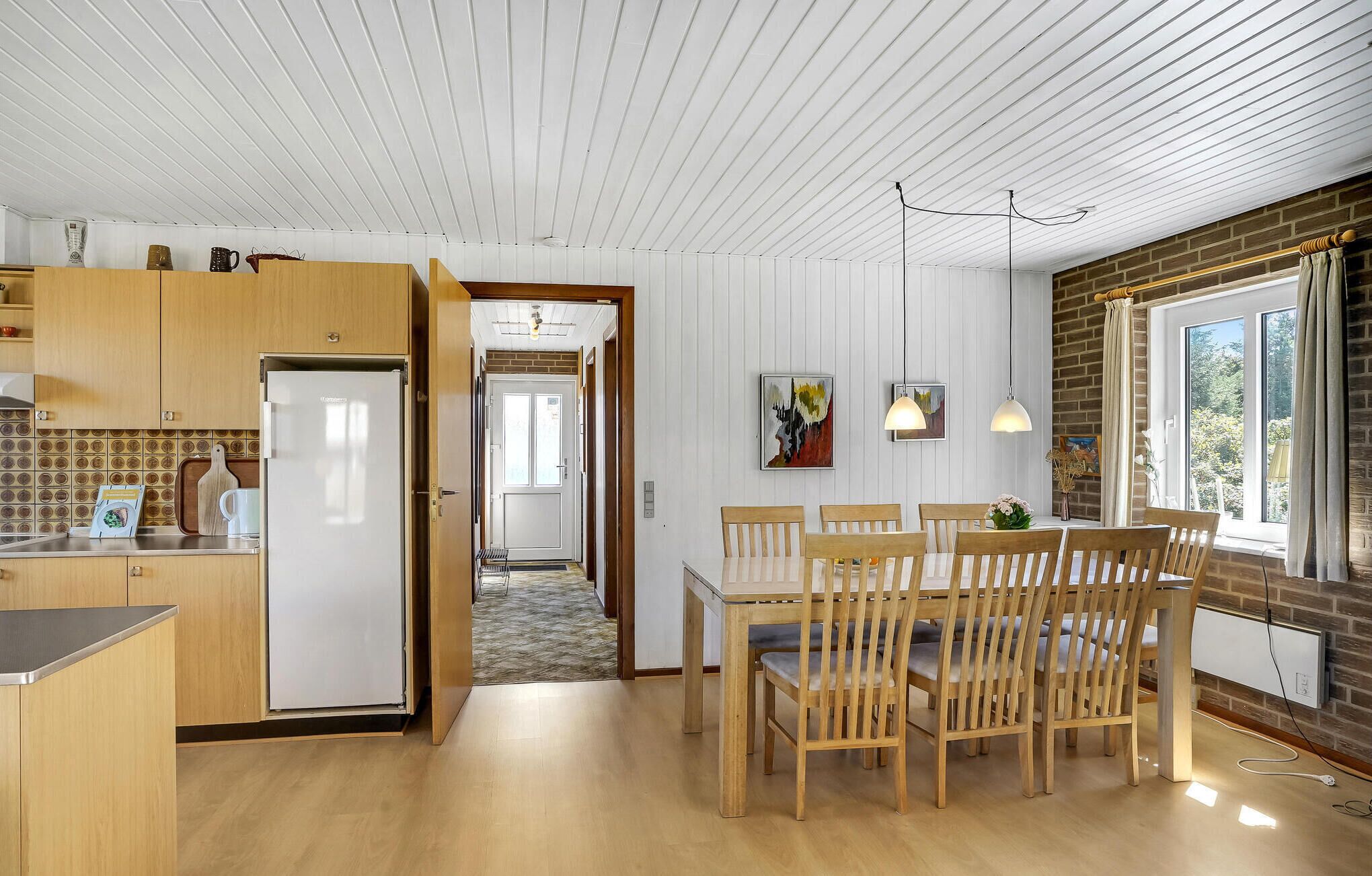 A modern kitchen with wooden cabinets, a built-in fridge, and a dining area with a wooden table and chairs.