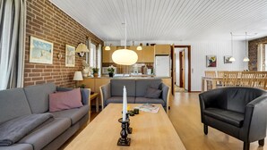 A modern living room with a brick wall, wooden ceiling, and a dining area with wooden furniture.