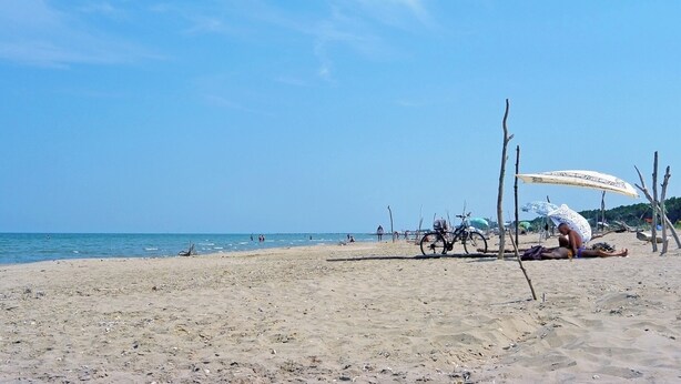 Ein Strand mit blauem Himmel, sandigem Ufer und einigen Personen sowie Fahrrädern.