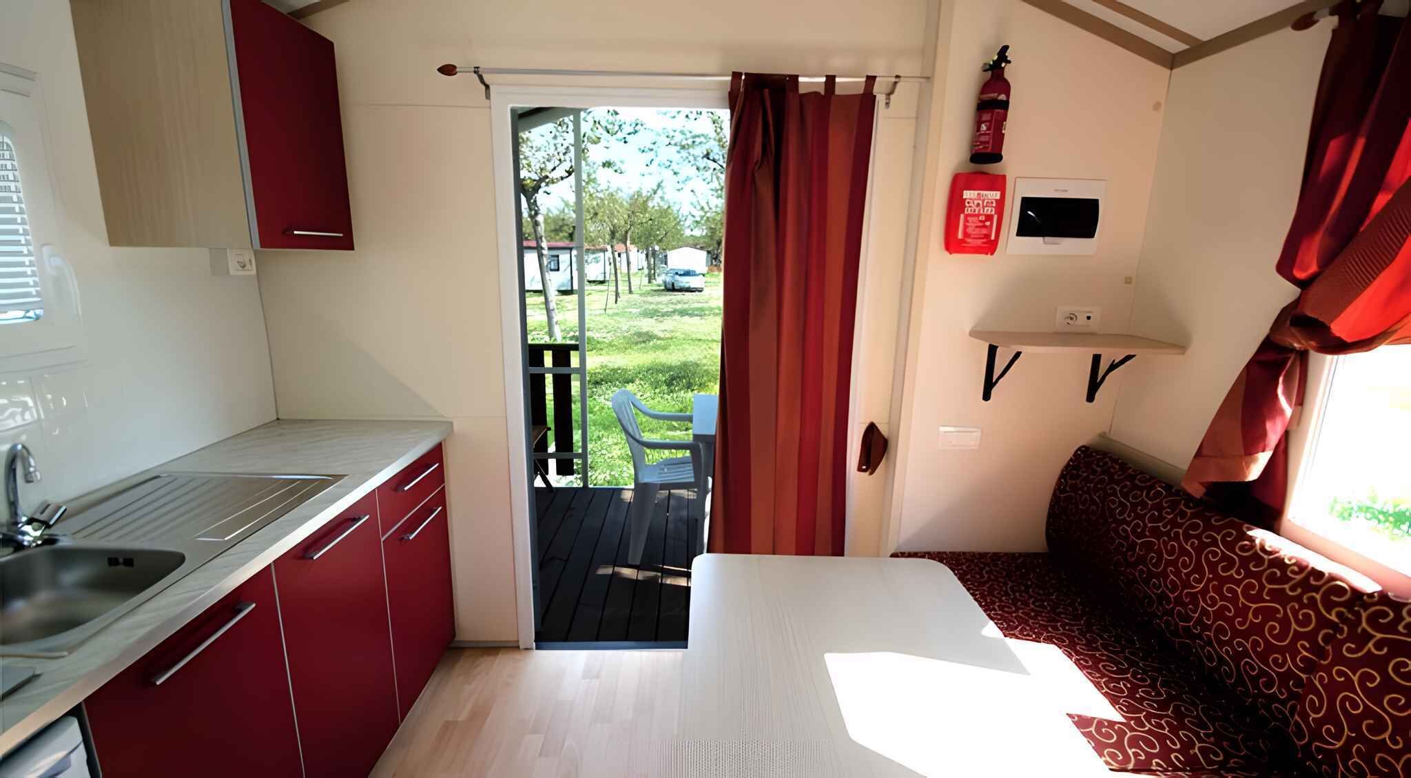 A compact kitchenette with a sink, cabinets, and a window overlooking a grassy area.