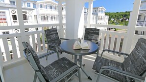 A balcony with white railings, a round table, and four chairs with black cushions.